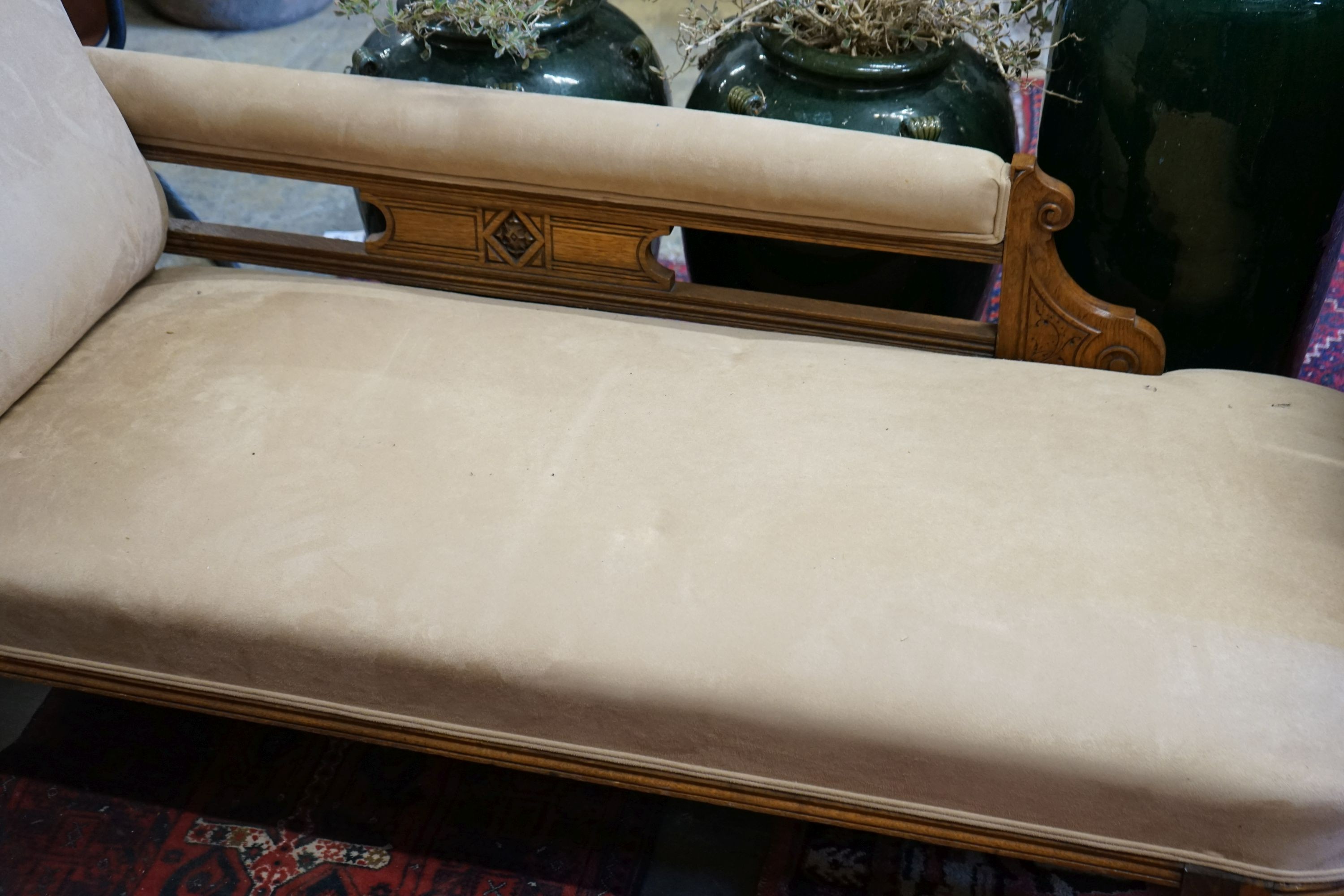 A late Victorian carved oak chaise longue upholstered in fawn suede, length 180cm, depth 70cm, height 79cm